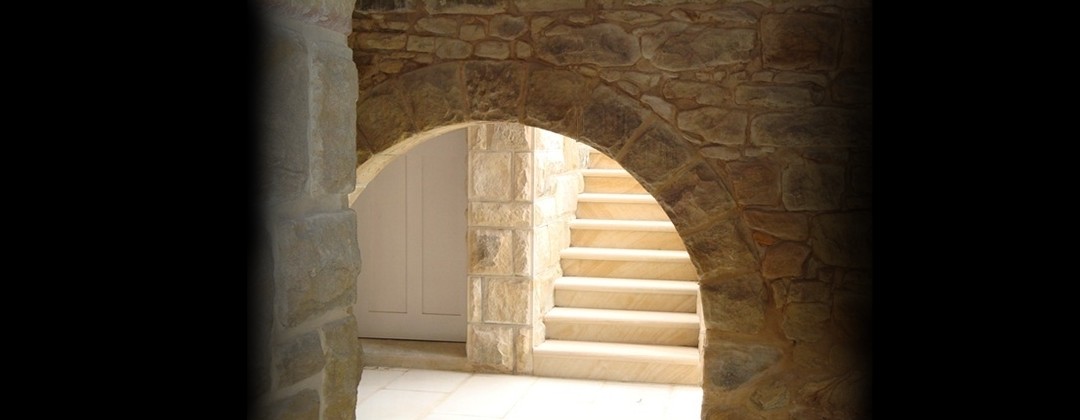 Flow of natural light from arch opening in sandstone wall leading to sandstone stairway.